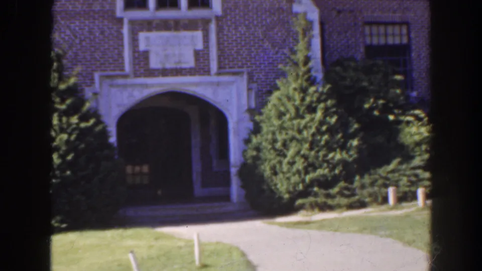 1941 Florida exterior view of a large brick building with a white-trimmed arched entrance, shrubs, lawn, and paved path.