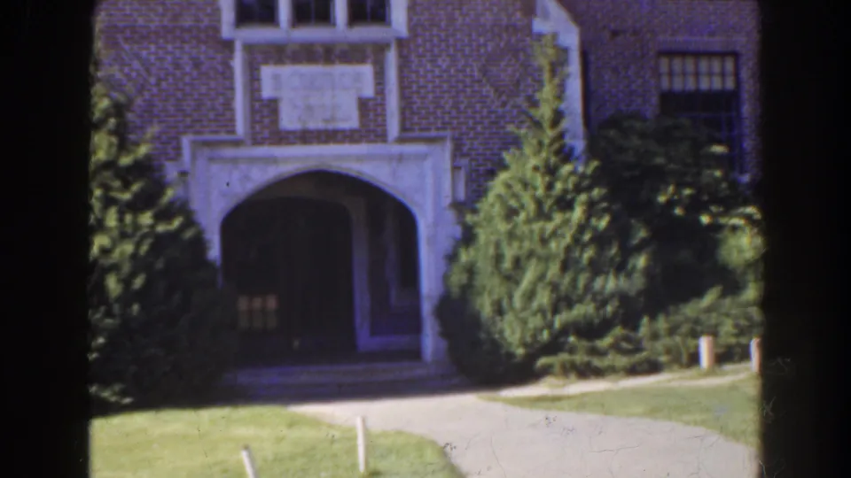 1941 Florida 8mm frame of the brick building's arched entry, flanked by dense greenery and a paved walk across the lawn.