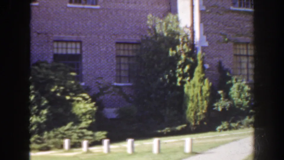 1941 Florida 8mm frame showing the house facade passing through the pan, with tall shrubs, windows, lawn, path, and white posts.