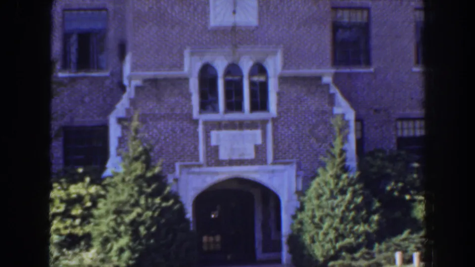1941 Florida 8mm frame showing a brick institutional-looking facade with white arched entry details and greenery in front.