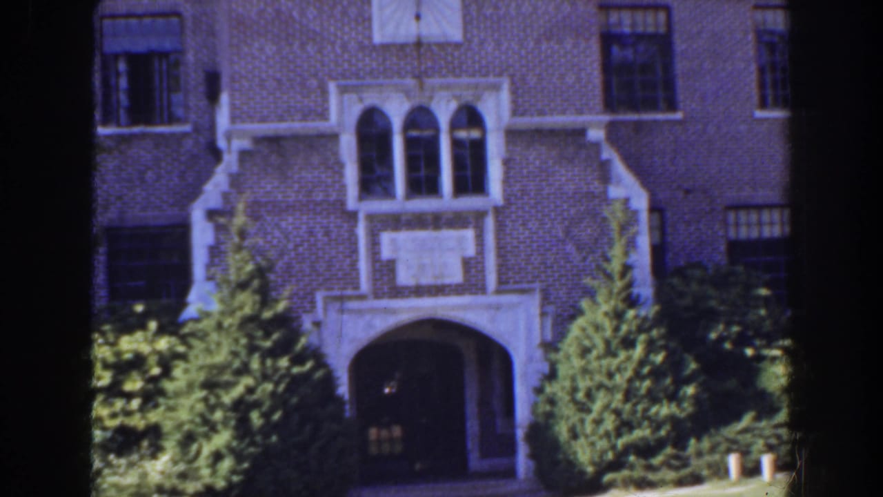1941 Florida home-movie frame with a brick building entrance, white decorative stonework, arched windows, and landscaped greenery.