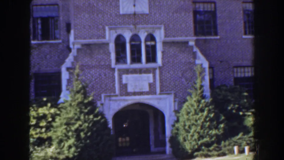 1941 Florida home-movie frame with a brick building entrance, white decorative stonework, arched windows, and landscaped greenery.