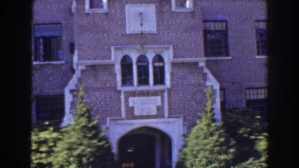 1941 Florida 8mm view of a brick building facade with a white arched entry, decorative window surround, and dense landscaping.