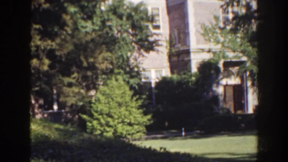 1941 Florida exterior showing a brick building entrance partly hidden by trees, with lawn, shrubs, and a partial car at the edge.