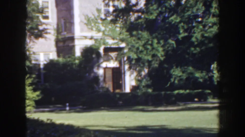 Late-frame 1941 Florida exterior showing clipped hedges, mature trees, and a large building beyond the lawn.