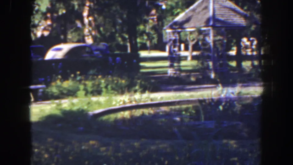 1941 Florida 8mm frame showing a wooden gazebo, parked cars, trees, grass, and a bright curved path.