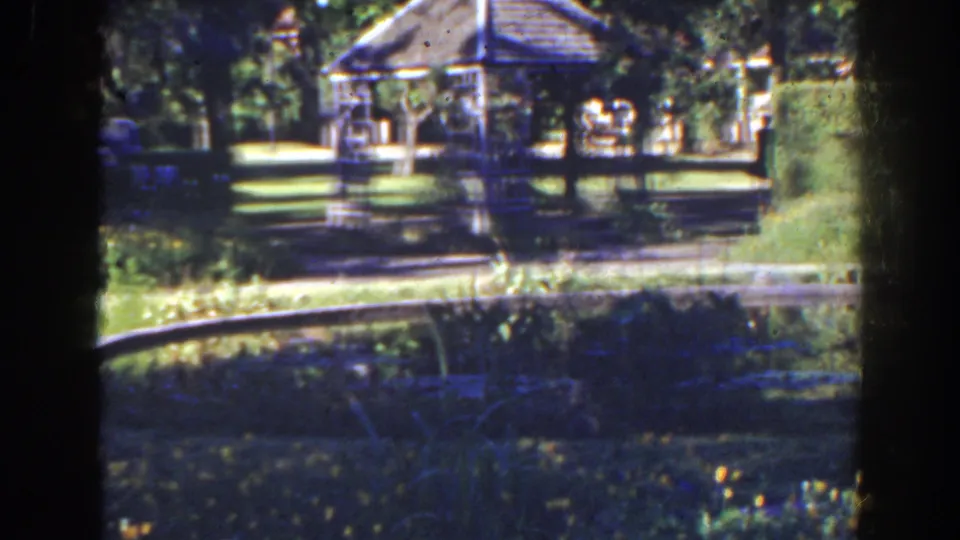 1941 Florida frame with a gazebo centered among trees, lawn, flowers, and a curving sunlit path.