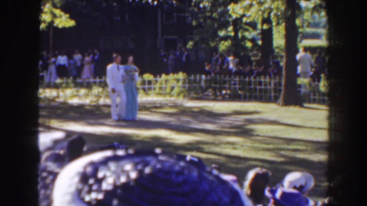 In 1941 Florida home-movie footage, a man in a white suit and a woman in a light blue gown walk past a fence and watching crowd.