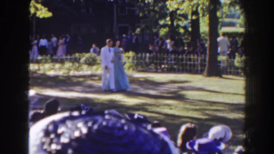 The couple moves along a shaded Florida garden aisle, with trees, a low white fence, and spectators visible in the background.