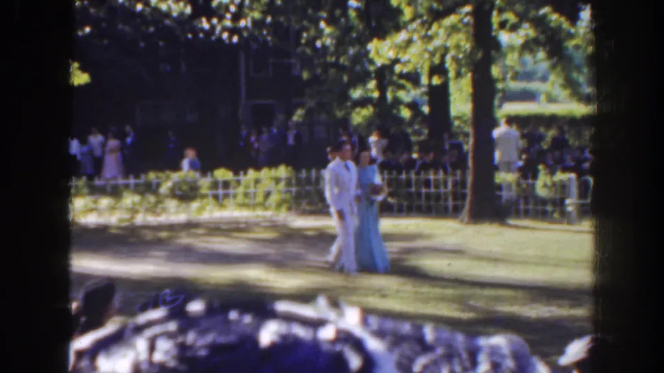 In 1941 Florida home-movie footage, a couple in formal attire walks through a sun-dappled park during an outdoor wedding gathering.
