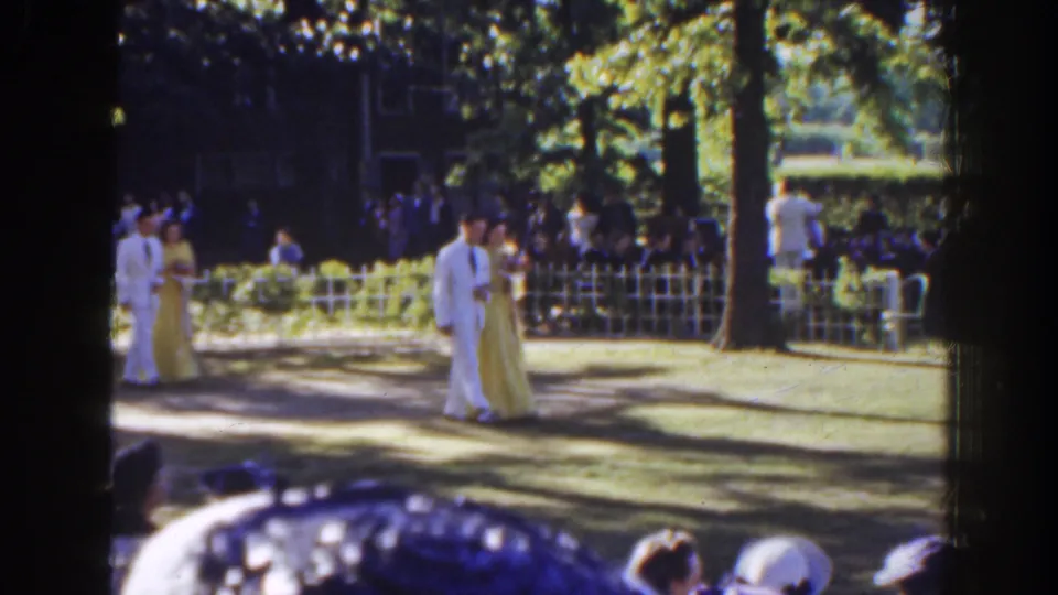 In 1941 Florida home-movie footage, a man in a white suit and a woman in a pale gown walk past a garden crowd.
