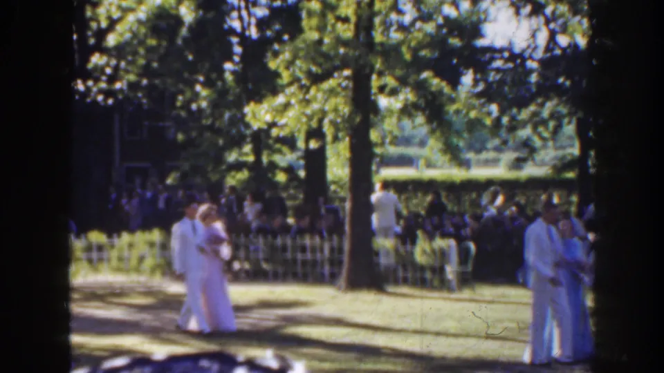 A formal couple is framed close to the foreground in the 1941 Florida garden scene, with guests and trees visible beyond.