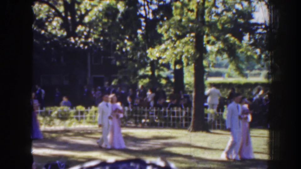 Bridesmaids in pale dresses pass through the Florida garden ceremony area as guests sit behind a low white fence.