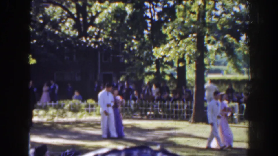 At the end of the 1941 Florida clip, couples continue walking past a guest crowd beside trees, fencing, and a large house.