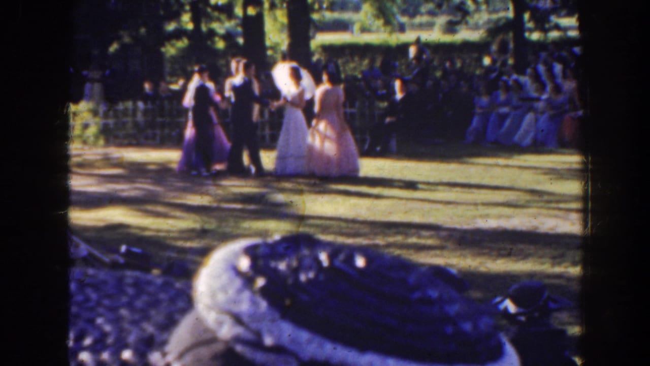 Wedding party walks or shifts together on the lawn with guests seated in the background.