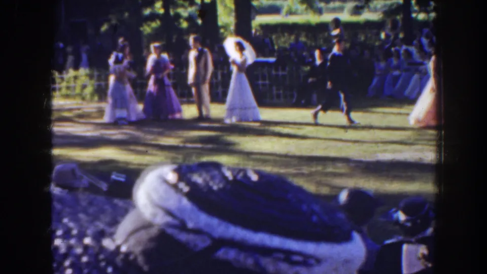 Home-movie frame of the 1941 Florida wedding party on a lawn, with a man in a dark suit walking in front of guests.