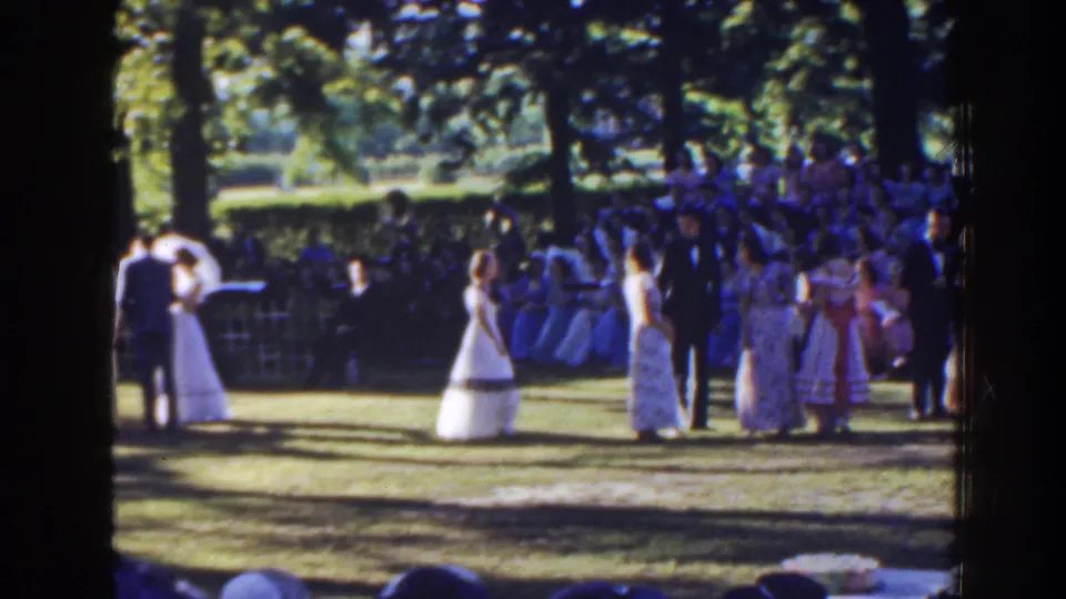 1941 Florida home-movie frame of the couple centered in a garden ceremony, with attendants and audience visible around them.