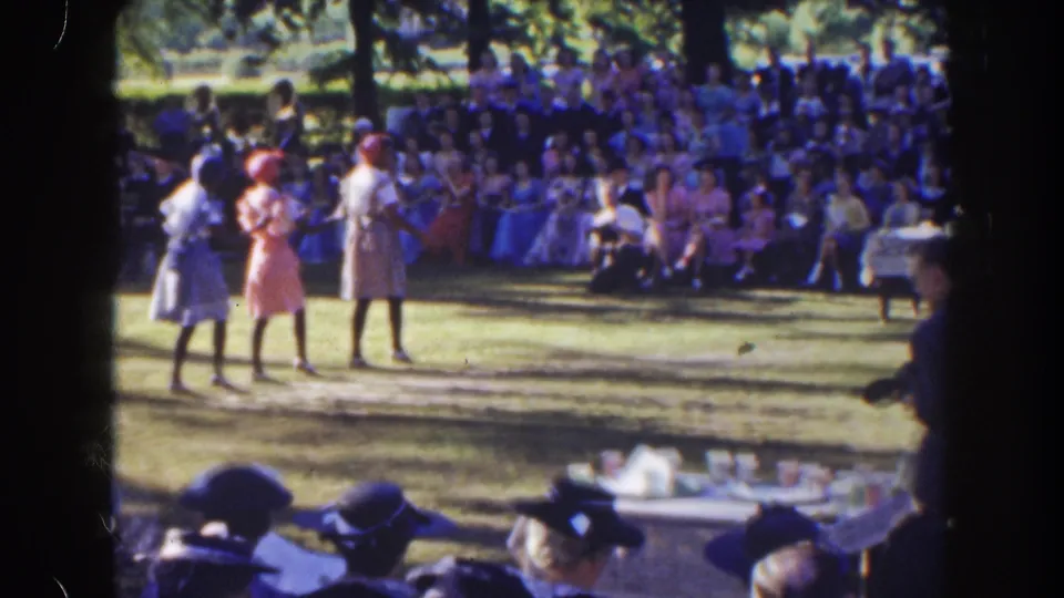 In 1941 Florida home-movie footage, three women in dresses stand or dance on a lawn before a seated outdoor audience.