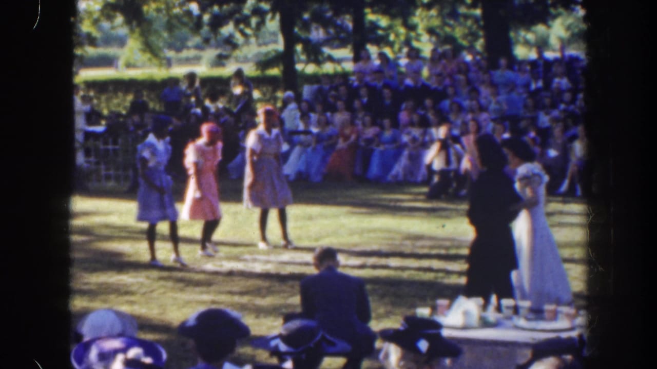Women dance on a lawn with a crowd seated behind them.