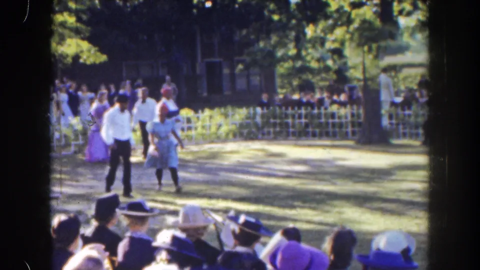 In 1941 Florida home-movie footage, four dressed participants cross a sunlit lawn before spectators in hats.