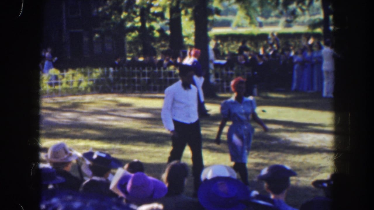 Man and woman walk across a lawn before a seated outdoor audience.