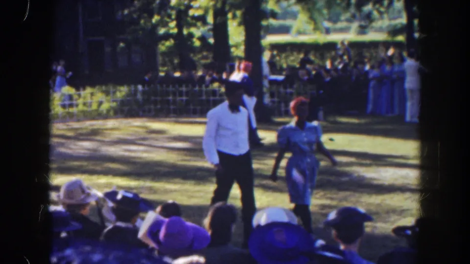 In 1941 Florida home-movie footage, a man in a white shirt and a woman in a light dress cross a grassy area as spectators watch.