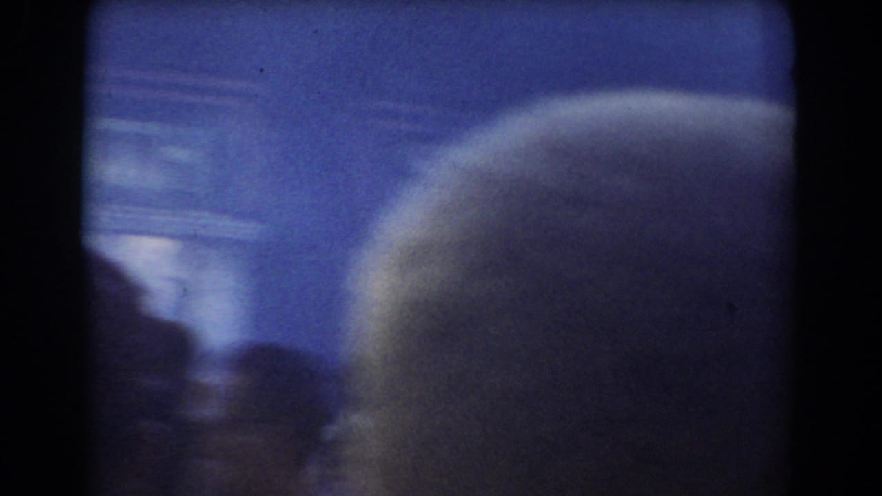Soft, blue-tinted 8mm frame from the York, Nebraska clip showing a partially obscured street view through a dark window frame.
