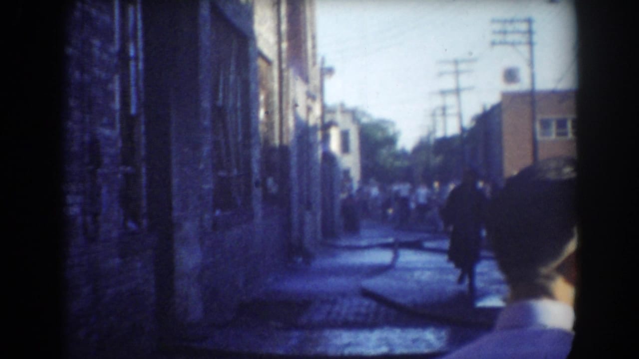 Wet narrow street with fire hoses, distant crowd and a man walking toward the camera.