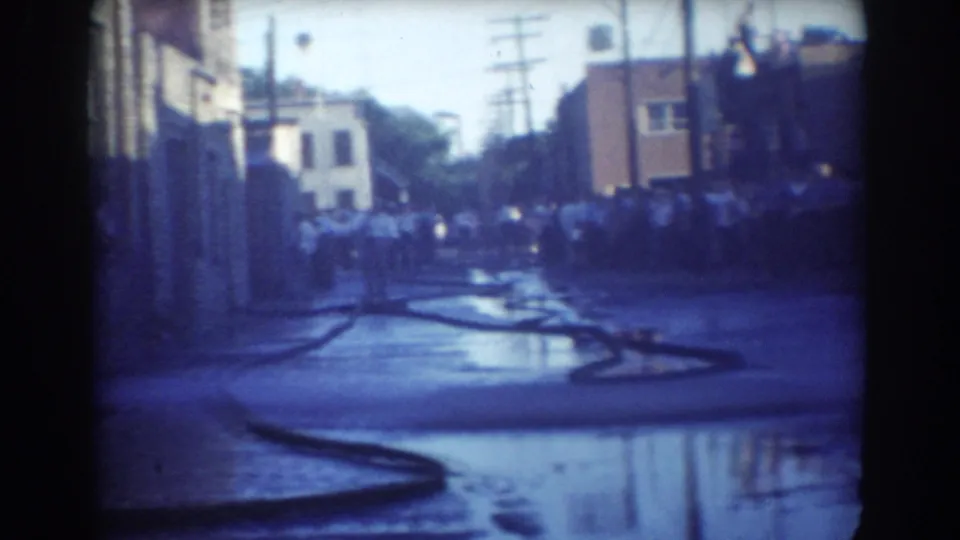 The 1958 York, Nebraska street scene shows a larger crowd beyond a hose lying across reflective pavement.