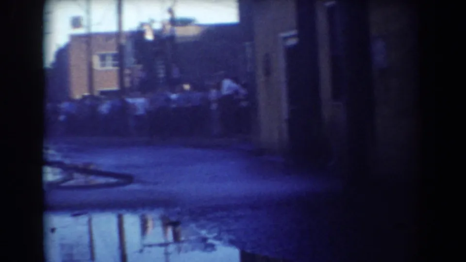 A distant crowd stands along a wet York, Nebraska street in 1958, with a hose crossing the foreground near building fronts.