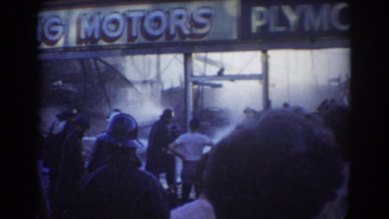 1958 York, Nebraska 8mm frame showing bystanders facing a smoky Plymouth Motors dealership as responders work near the front windows.