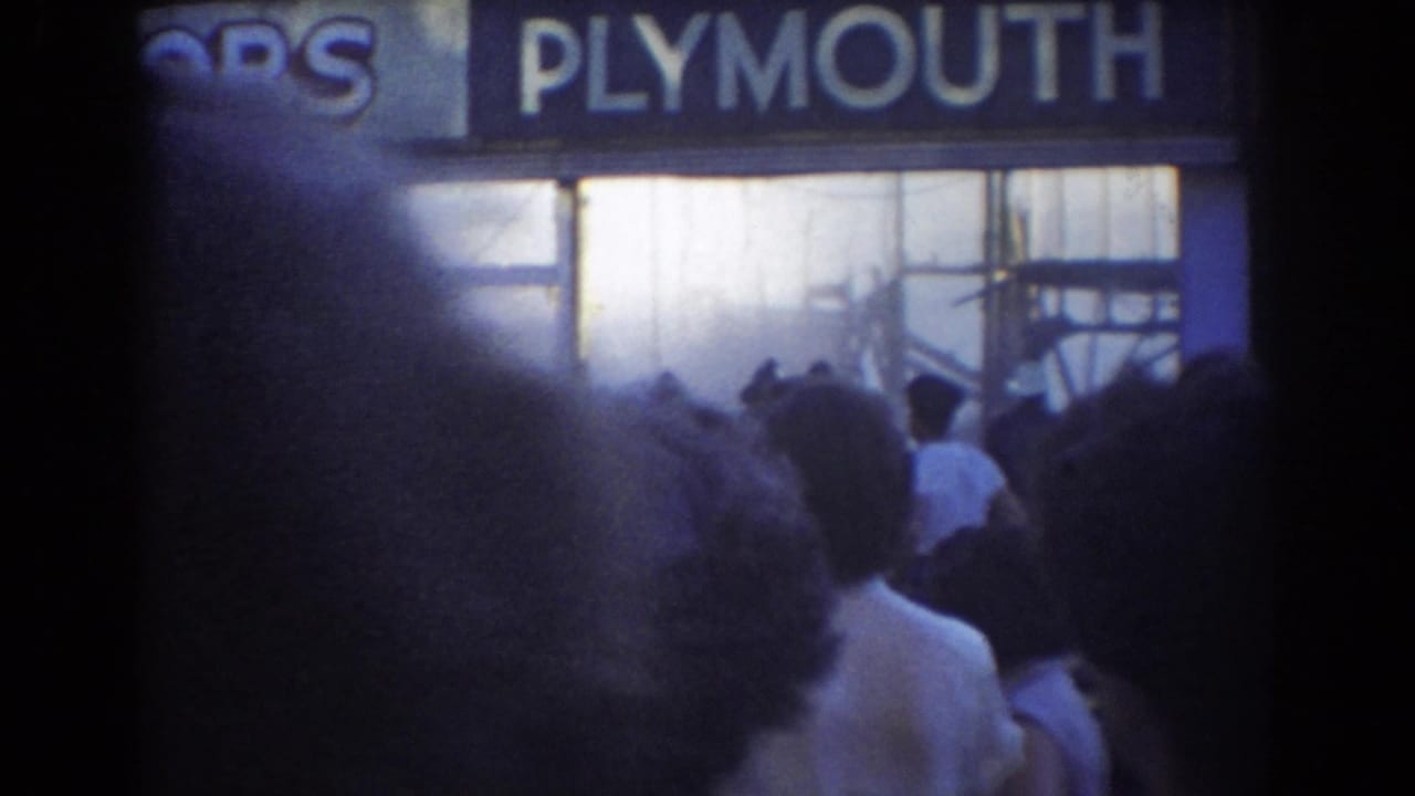 Onlookers stand before a smoky Plymouth storefront with spray at the windows.
