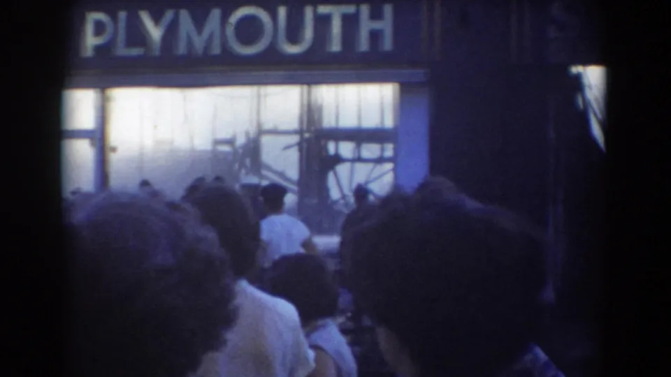 8mm frame of the Plymouth Motors sign and smoke-filled windows, with bystanders in the foreground during the 1958 York, Nebraska fire.