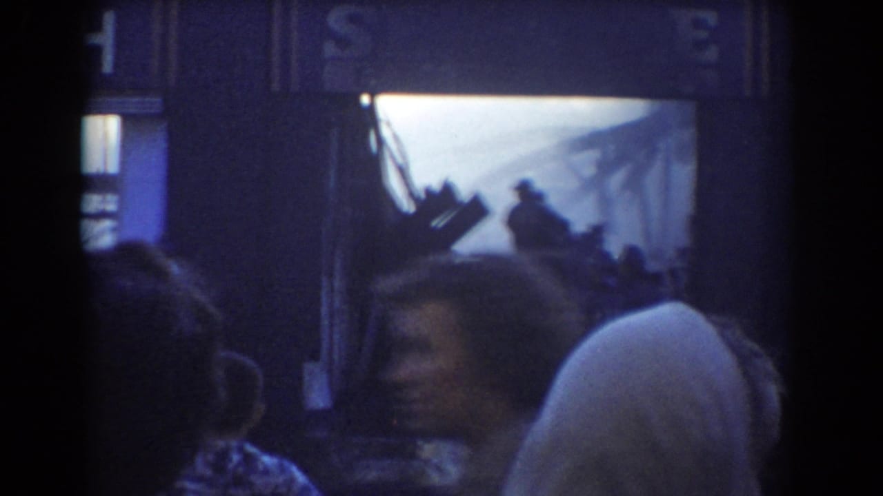Crowd silhouettes watch a bright fire scene near a building front.