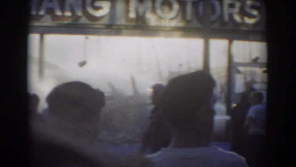 York, Nebraska 1958 home-movie frame with onlookers in front of a storefront where MOTORS lettering is visible above bright windows.