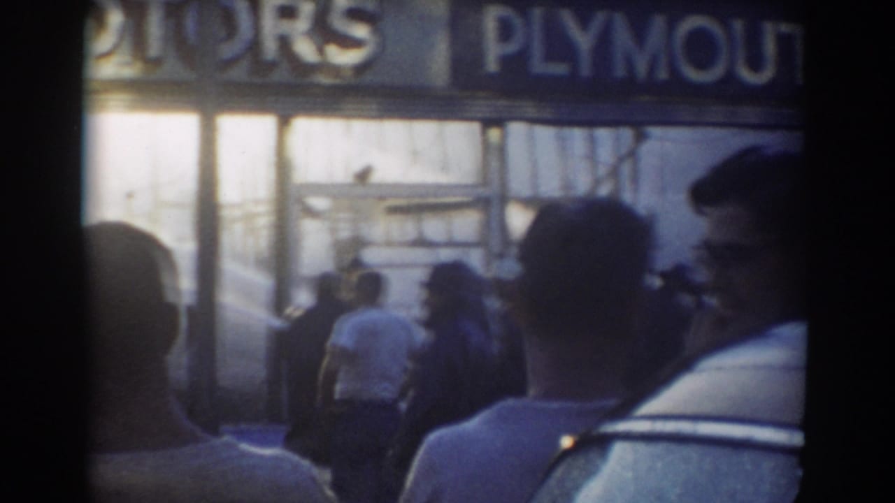 Crowd outside a storefront with a partially visible Plymouth sign above the entrance.