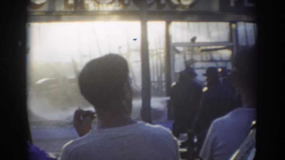 In York, Nebraska 1958 home-movie footage, adults stand with backs to camera watching a strong water spray in a bright worksite setting.