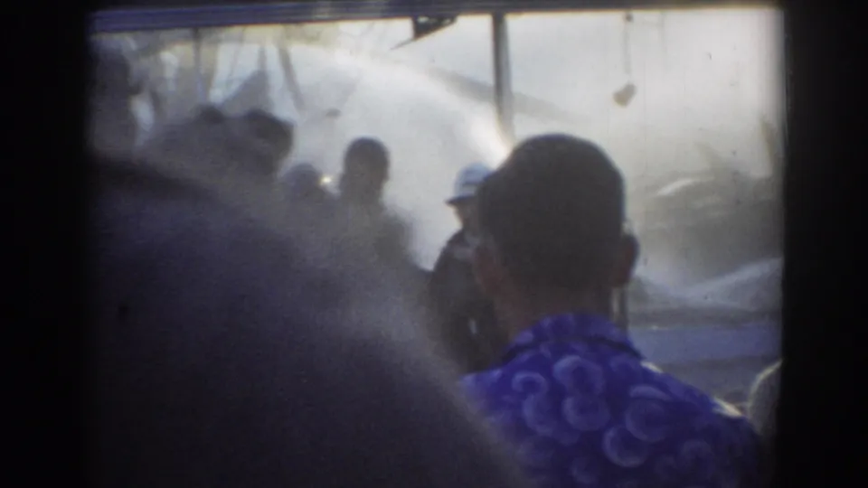 The handheld 8mm view is partially obscured by nearby spectators while mist from the hose operation fills the York, Nebraska scene.