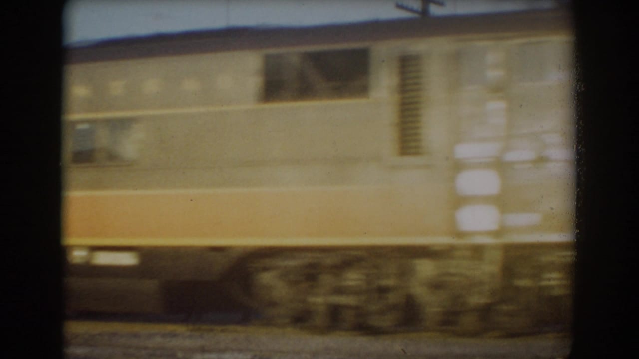 Orange-and-cream train car passing beside tracks, blurred by motion.
