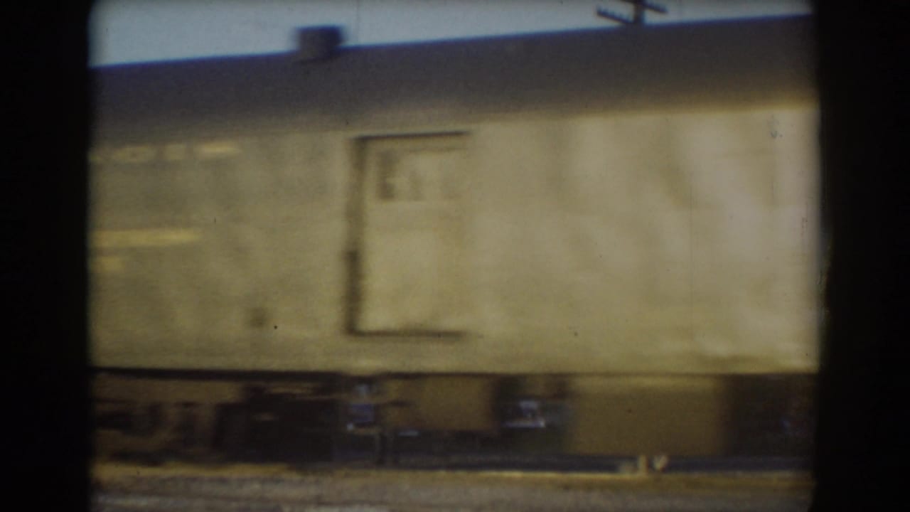 Light-colored train car side passes through York, Nebraska, with a door outline, small window, and undercarriage visible in soft 8mm motion blur.