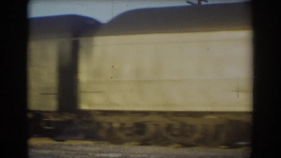 Pale passenger car body in the 1958 York, Nebraska train sequence, with roofline, wheel area, and trackside ground softened by motion.