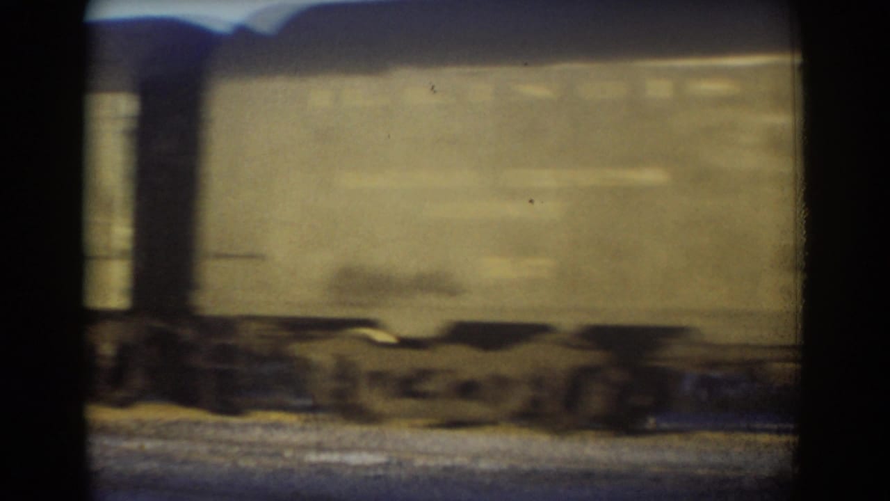 Beige freight car passing on tracks with wheels visible below.