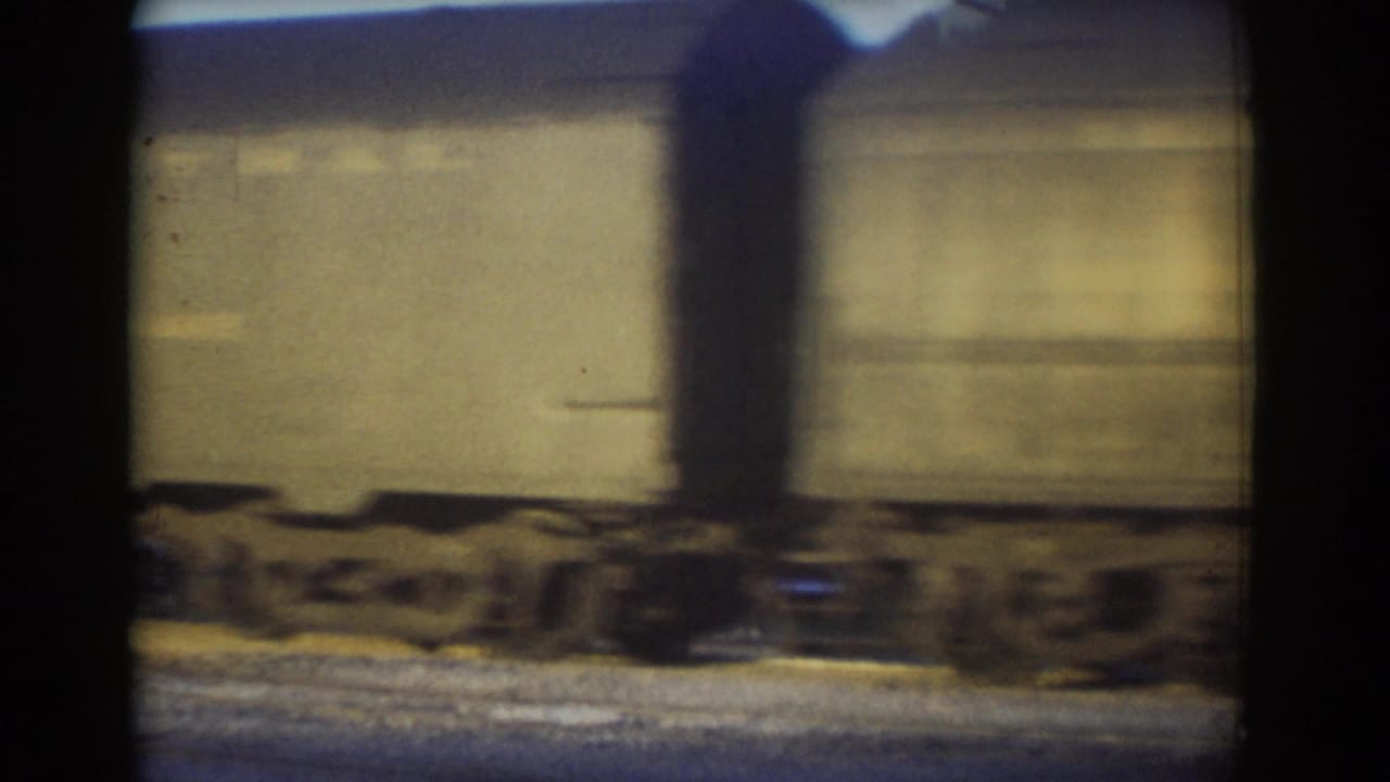 A motion-blurred beige freight car rolls along rail tracks in 1958 York, Nebraska footage.