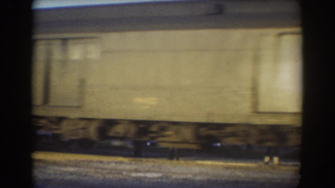 A blurred rail car passes beside tracks with wheels and gravel visible below.