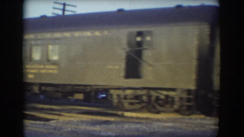 1958 York, Nebraska 8mm frame showing a moving rail car with windows, a side door, partial lettering, wheels, and utility poles behind it.