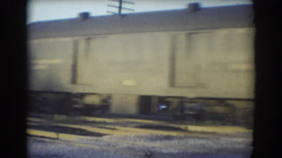 1958 York, Nebraska frame of a pale moving rail car with undercarriage, tracks, gravel, and utility poles visible through 8mm film blur.