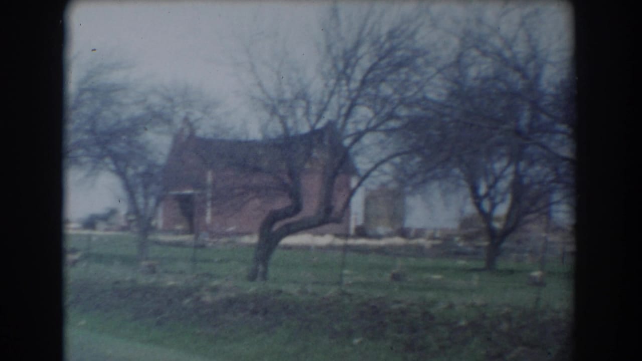 Detached brick building behind grass, wire fencing, and bare trees.