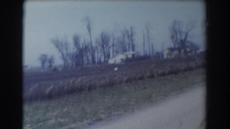 1958 York, Nebraska 8mm frame showing a rural roadside field with distant houses, bare trees, and a pale overcast sky.
