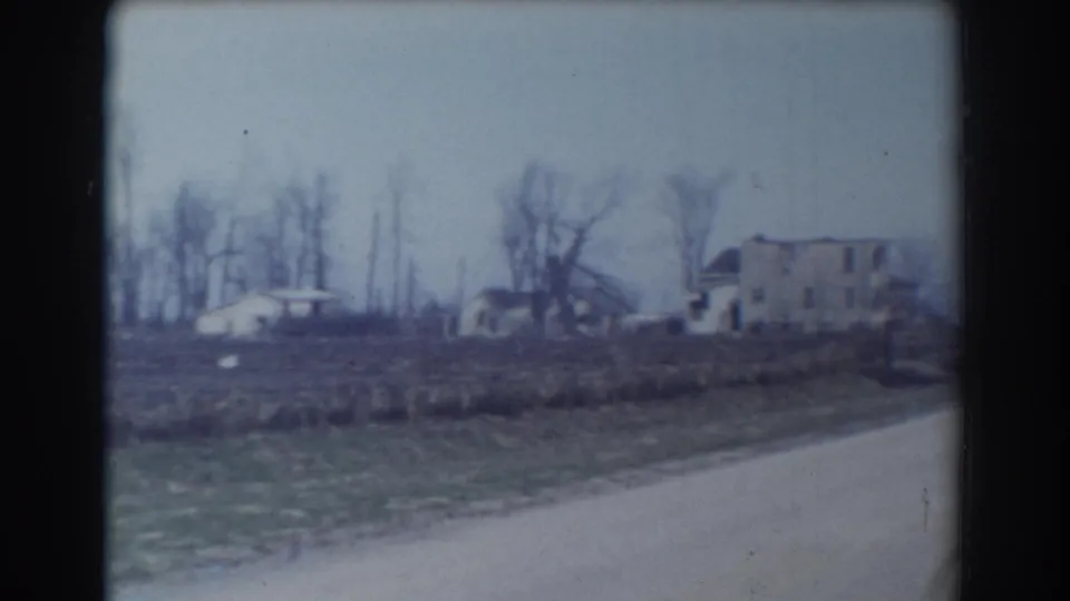 1958 York, Nebraska rural view with two distant houses, a low outbuilding, bare trees, and a pale road edge.