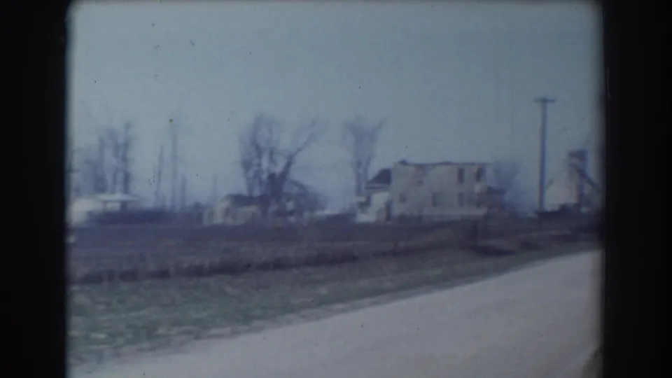 Late-1950s York, Nebraska frame showing a pale house, utility pole, bare trees, open field, and dirt road.